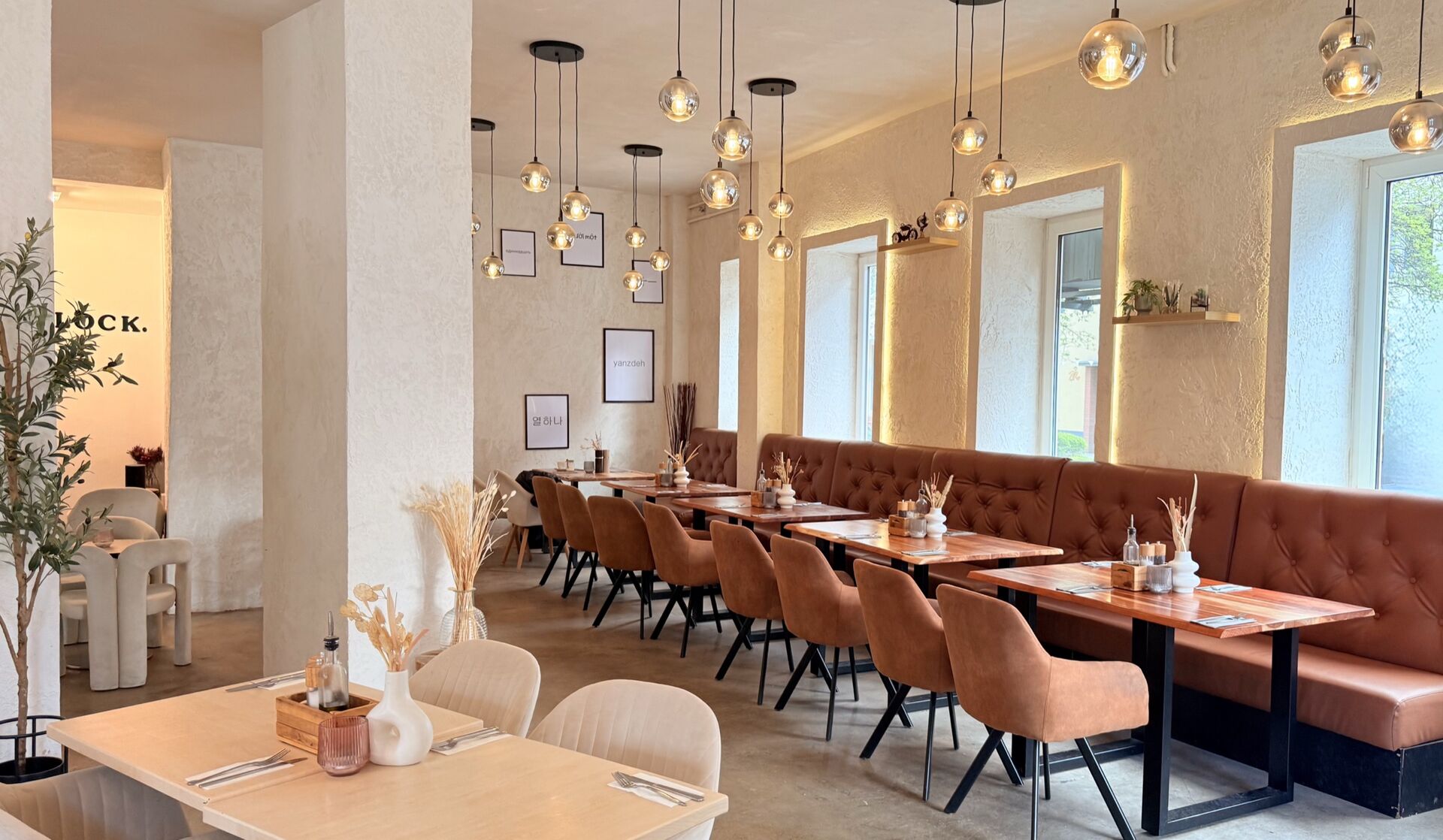 Warmer Innenraum des ELEVEN Brunch & Café in Kiel mit beigen Velours-Stühlen, Cognac-Leder-Bank und Messing-Hängeleuchten